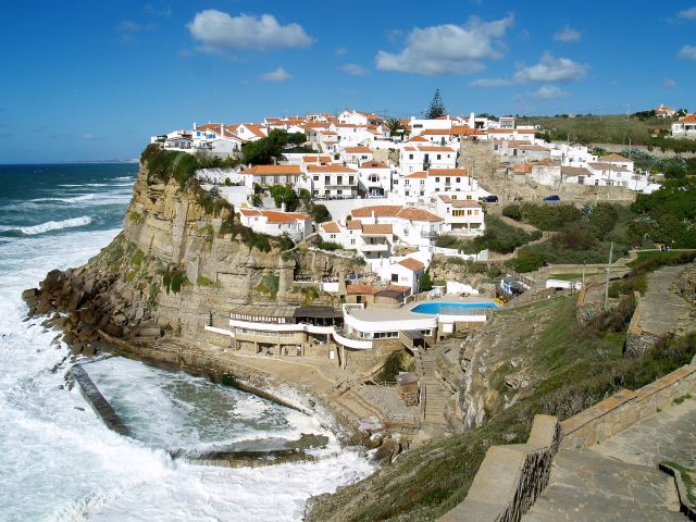 Weiß getünchte Häuser mit roten Dächern in einem malerischen Dorf an der Atlantikküste Portugals. Auf einer Klippe sind sie relativ sicher, aber neue Gebäude liegen auf Meeresniveau.