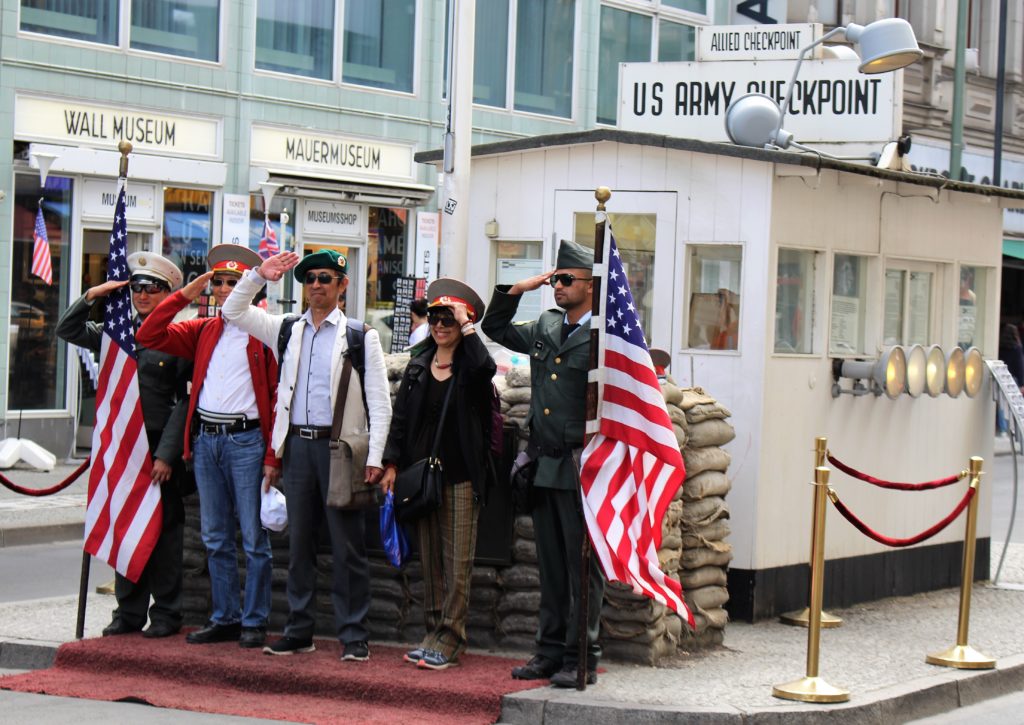 Vier Besucherinnen und Besucher salutieren mit zwei Fake-US-Soldaten am Checkpoint Charlie.