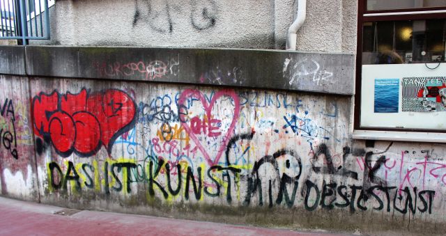 'das ist Kunst mindestens' steht in krakeligen Buchstaben an einer Wand mit Graffiti.