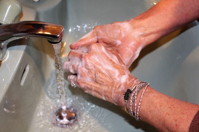 Zwei Hände mit Seife über Waschbecken (grüne Farbe).