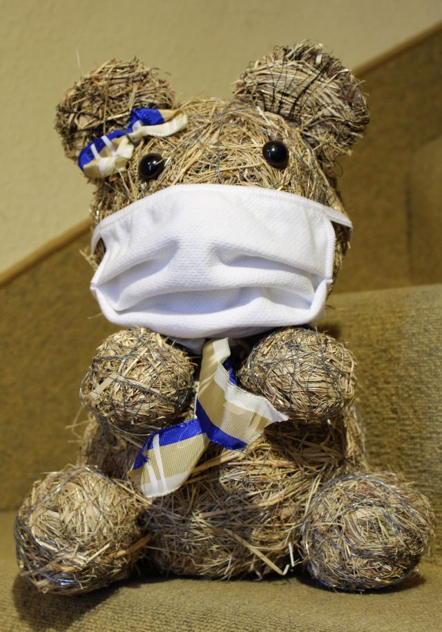 Ein Bär aus Heu mit einer weißen Schutzmaske über Mund und Nase.