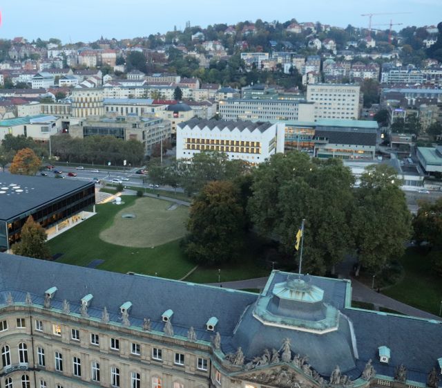 Blick aus einem Riesenrad auf das flache Landtagsgebäude, das Neue Schloss mit der baden-württembergischen Fahne, Haus der Abgeordneten und Landesbibliothek.