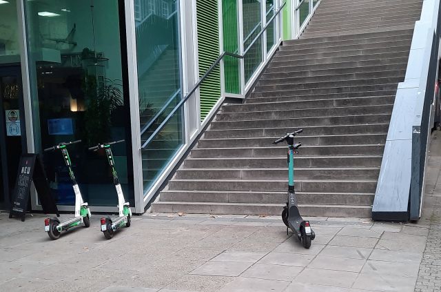 Ein E-Scooter steht vor einer langen Treppe, zwei daneben.