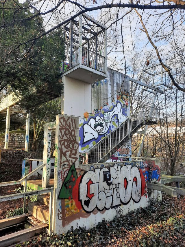 Ein Treppenhaus aus hellem Beton mit Treppen ins Nirgendwo. Alles ist mit Graffiti verschmiert.
