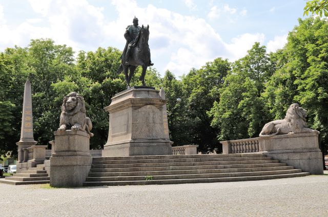 Kaiser Wilhelm I. hoch zu Ross in Metall gefertigt auf einem hohen Sockel. Der Zugang erfolgt über Stufen. Links und rechts ein liegender Löwe.