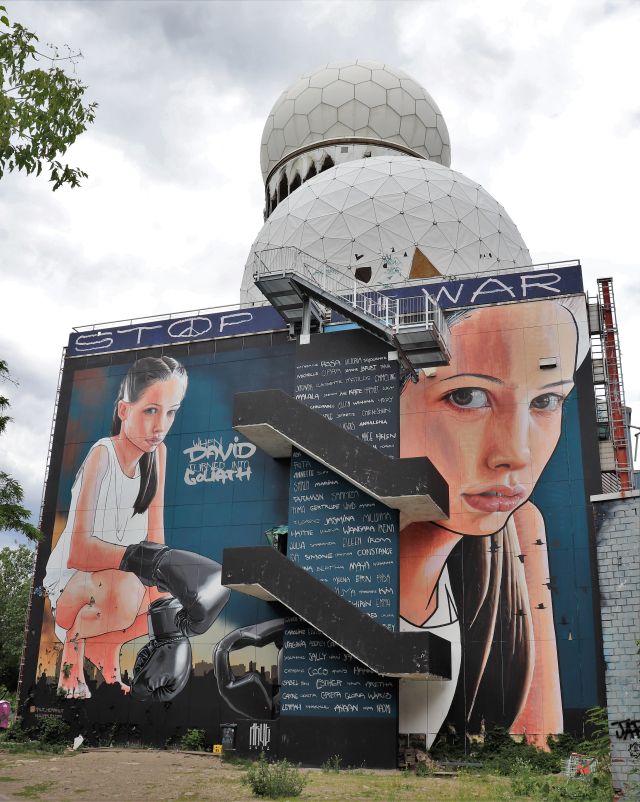 Großformatiges Gemälde auf einer Hausfassade. Es zeigt eine junge Frau mit Boxhandschuhen. Text "When David turned into Goliath". Darüber "Stop War".