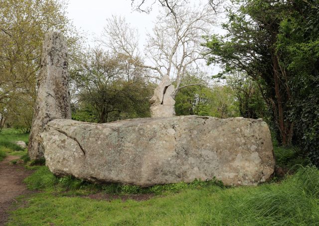 Ein gewaltiger Granitblock liegt im Vordergrund, dahinter zwei sehr hohe Menhire stehend.