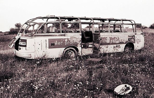 Ein Schwarz-Weiß-Foto zeigt einen zerfallenden Bus auf einer Wiese.
