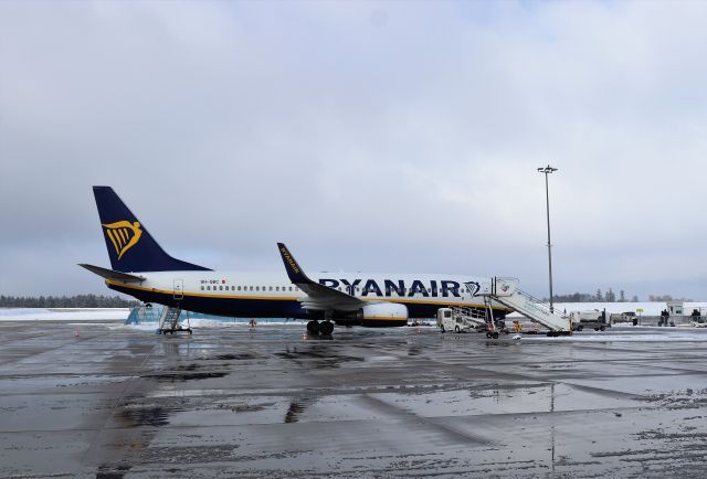 Weiß-blaues Flugzeug von Ryanair steht mit Gangway auf dem nassen Vorfeld.
