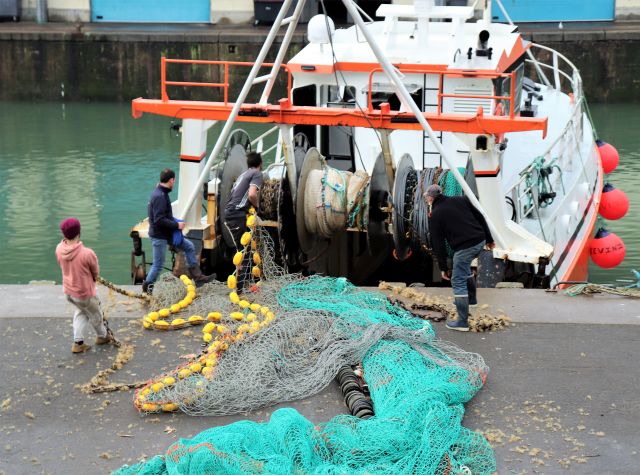 Ein Fischtrawler liegt am Kai. Man sieht das ausgerollte grüne Netz.
