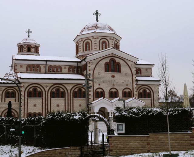 Ein Gebäude in weiß-rot gehaltenen Farben. Es ist eine griechisch-orthodoxe Kirche mit mehreren Kreuzen auf dem Dach.