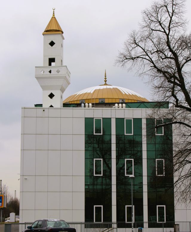 Ein helles Gebäude mit grünlichen Teilen, darüber ein schmales Türmchen und ein gewölbtes golden glänzendes Dach. Eine Moschee in Esslingen.