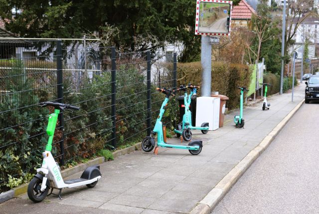 Grün-weiße E-Scooter, eine Art Tretroller mit Elektroantrieb, stehen kreuz und quer auf einem Gehweg.
