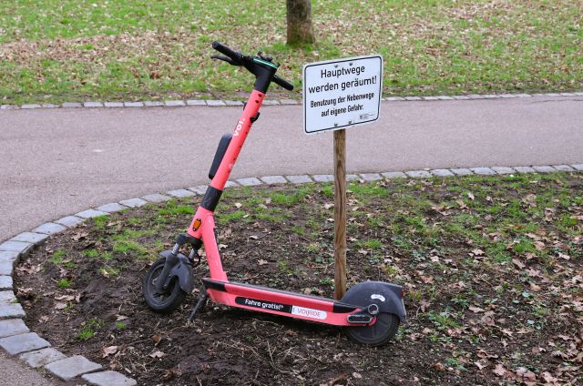 Roter E-Scooter lehnt im Rosensteinpark an einem Pfahl mit dem Schild "Hauptwege werden geräumt. Benutzung der Nebenwege auf eigene Gefahr".