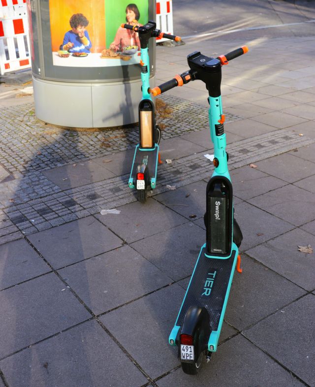Zwei grüne E-Scooter stehen leicht versetzt hintereinander mitten auf dem Gehweg.