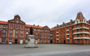 Ein Gebäude aus roten Bachsteinen, drei Stockwerke hoch. In der Mitte des Vorplatzes steht eine Skulptur aus Metall, sie zeigt Jean-Baptiste André Godin.